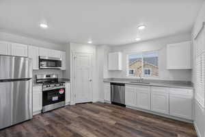 Kitchen featuring stainless steel appliances, white cabinetry, and dark wood-style floors
