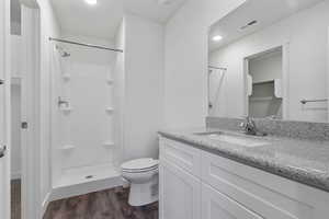 Bathroom with a spacious closet, vanity, dark wood-style floors, a stall shower, and recessed lighting