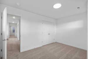 Unfurnished bedroom featuring light carpet and a closet