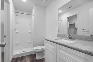 Full bathroom with vanity, a spacious closet, a shower stall, dark wood-type flooring, and recessed lighting