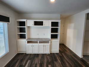 Unfurnished living room featuring dark wood-style flooring and baseboards