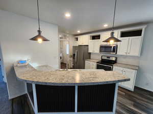 Kitchen with a peninsula, appliances with stainless steel finishes, white cabinetry, decorative light fixtures, and tasteful backsplash