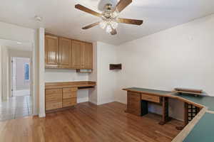 Unfurnished office with built in desk, light wood-style floors, and a ceiling fan