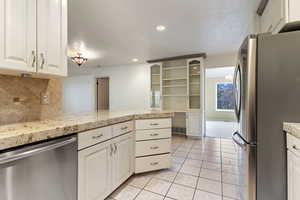 Kitchen featuring appliances with stainless steel finishes, light countertops, white cabinets, a peninsula, and decorative backsplash