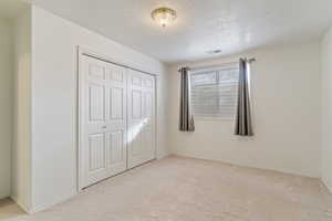 Unfurnished bedroom with a textured ceiling, light colored carpet, and a closet