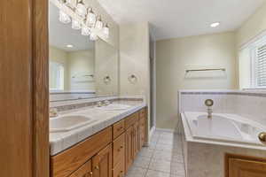 Bathroom featuring a tub with jets, double vanity, light tile patterned floors, and recessed lighting