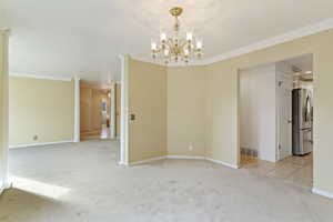 Unfurnished dining area featuring light carpet, a chandelier, ornate columns, and crown molding