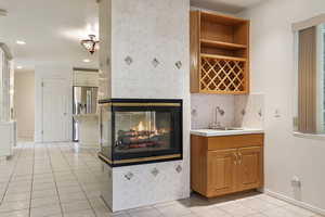 Indoor wet bar with a tile fireplace, light tile patterned floors, light countertops, open shelves, and stainless steel fridge with ice dispenser