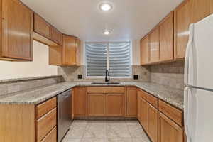 Kitchen with freestanding refrigerator, light stone countertops, stainless steel dishwasher, and decorative backsplash