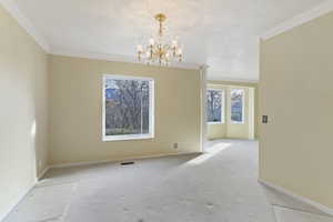 Empty room featuring crown molding, a chandelier, and carpet flooring
