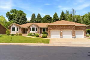 Stone veneer and stucco exterior residence featuring a three-car garage, bay windows, and a landscaped front yard with mature trees