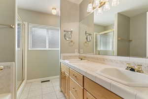 Full bathroom with double vanity, a stall shower, and light tile patterned floors