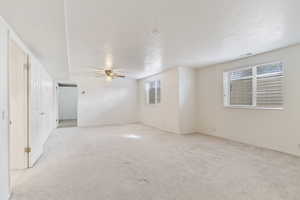 Unfurnished room featuring light colored carpet, a ceiling fan, and healthy amount of natural light