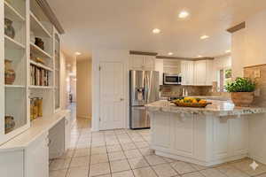 Kitchen with a peninsula, stainless steel appliances, white cabinets, open shelves, and light tile patterned floors
