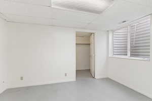 Unfurnished bedroom featuring a walk in closet, concrete floors, and a drop ceiling