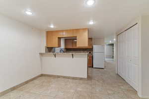 Kitchen with freestanding refrigerator, brown cabinetry, a peninsula, a kitchen bar, and decorative backsplash
