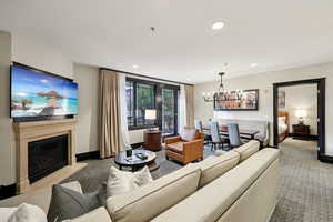 Living room with carpet, a glass covered fireplace, a chandelier, and recessed lighting