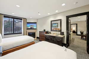 Bedroom with dark colored carpet, a glass covered fireplace, and recessed lighting