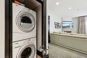 Laundry area with stacked washer and clothes dryer, recessed lighting, light carpet, and a fireplace