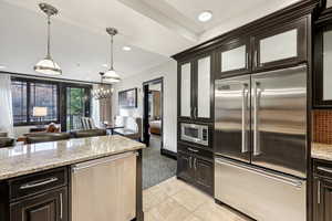 Kitchen with built in appliances, light stone counters, decorative light fixtures, dark brown cabinets, and a chandelier