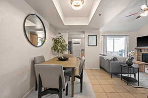 Dining space featuring light tile patterned floors, a stone fireplace, a raised ceiling, and a chandelier