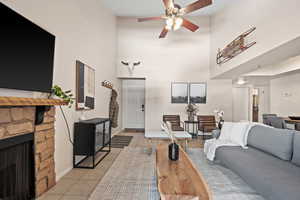 Living room featuring a high ceiling, light tile patterned floors, ceiling fan, and a stone fireplace