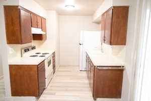 Kitchen with white appliances, light countertops, under cabinet range hood, and light wood-type flooring
