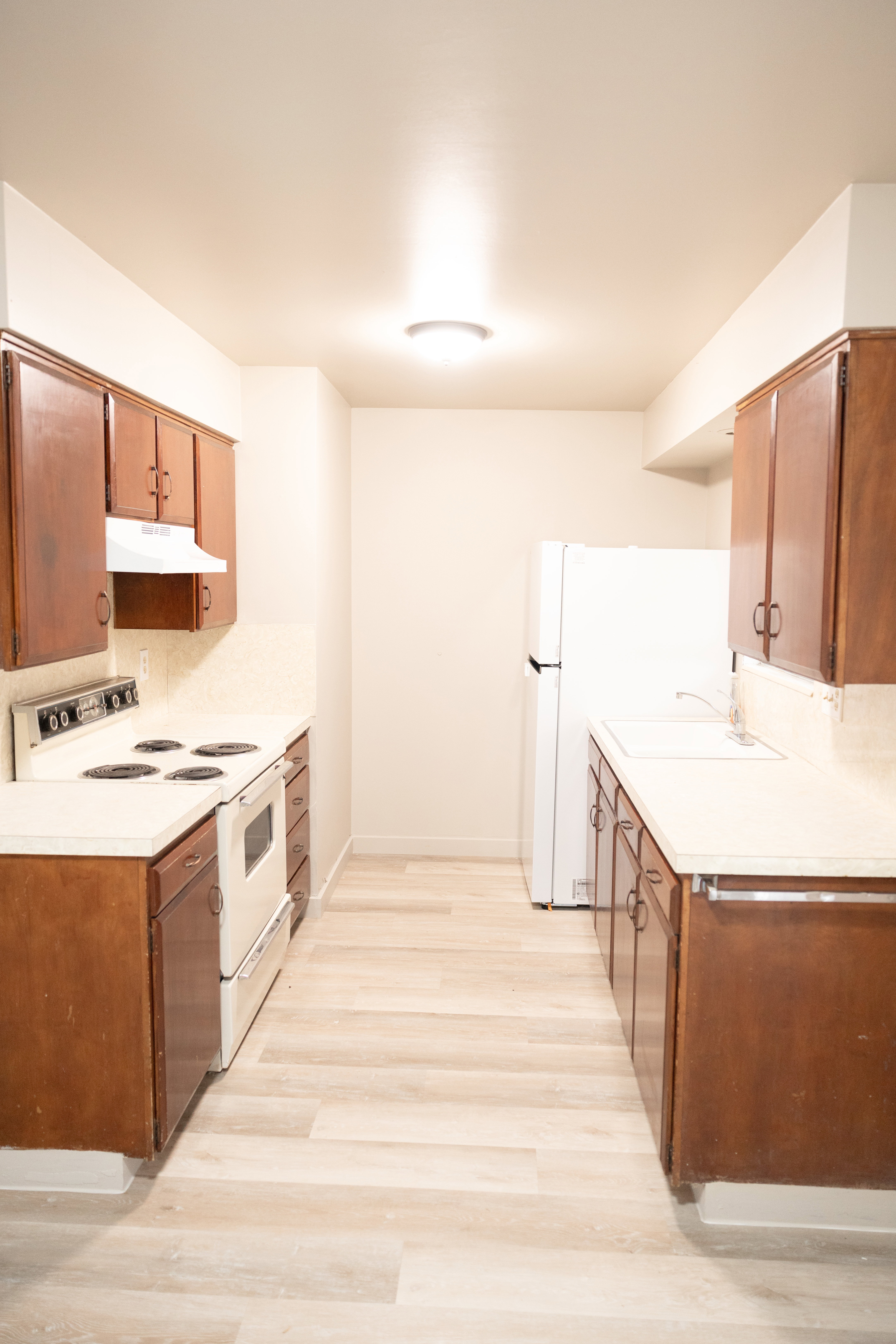 Kitchen with white appliances, light countertops, brown cabinetry, and light wood-style floors