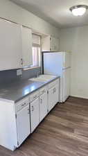Kitchen with white cabinets, freestanding refrigerator, dark wood-style flooring, and dark countertops
