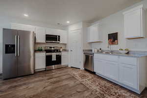 Kitchen with stainless steel appliances, white cabinets, dark wood-style flooring, recessed lighting, and light stone counters