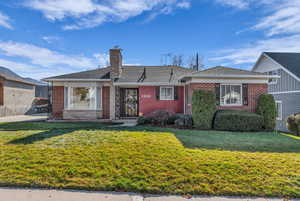 View of front of home with brick siding, a chimney, a front yard, and a shingled roof
