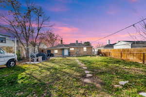 Back of property at dusk featuring brick siding, a patio area, a chimney, and a fenced backyard
