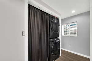 Washroom featuring stacked washing machine and dryer, dark wood-style floors, and recessed lighting