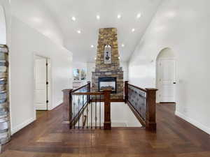 Corridor featuring high vaulted ceiling, an upstairs landing, arched walkways, recessed lighting, and dark wood-style flooring