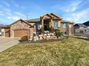 View of front of property featuring driveway, a garage, a front lawn, and stone siding