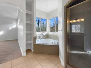 Full bathroom with built in shelves, a bath, light colored carpet, light tile patterned floors, and healthy amount of natural light