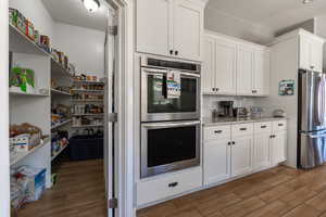 Kitchen featuring appliances with stainless steel finishes, white cabinets, wood finish floors, and light stone countertops