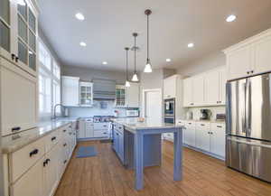 Kitchen with glass insert cabinets, white cabinets, appliances with stainless steel finishes, a breakfast bar area, and pendant lighting