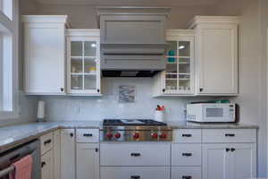 Kitchen featuring white cabinetry, appliances with stainless steel finishes, glass insert cabinets, and light stone counters