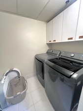 Washroom featuring light tile patterned flooring, washing machine and dryer, and cabinet space