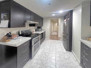 Kitchen featuring stainless steel appliances, under cabinet range hood, light tile patterned floors, light stone counters, and recessed lighting