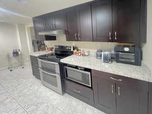 Kitchen featuring appliances with stainless steel finishes, light stone countertops, and under cabinet range hood