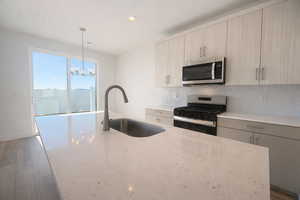 Kitchen with stainless steel appliances, backsplash, modern cabinets, light stone countertops, and light wood-style floors