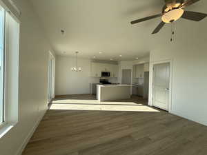 Unfurnished living room featuring dark wood-style floors, recessed lighting, a chandelier, and ceiling fan