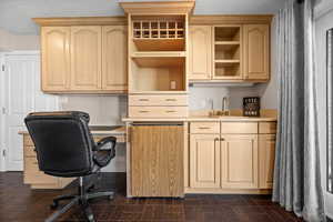 Office area in basement family room featuring desk, cabinetry, went bar & mini fridge