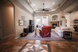 Living area featuring a tray ceiling, inlaid floor details, a ceiling fan, a tile fireplace, and recessed lighting
