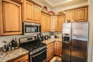 Kitchen featuring appliances with stainless steel finishes, light stone countertops, and brown cabinets