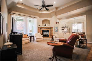 Living room with a raised ceiling, a tile fireplace, a ceiling fan, a chandelier, and recessed lighting