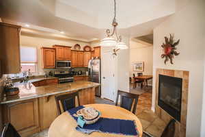 Kitchen featuring brown cabinets, light stone counters, a tile fireplace, pendant lighting, and stainless steel appliances