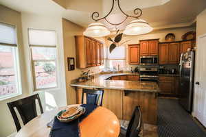 Kitchen featuring dark stone counters, appliances with stainless steel finishes, hanging light fixtures, a peninsula, and a breakfast bar